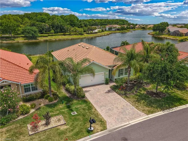 Waterfront property featuring a tile roof, paved driveway, mature palm trees, and established landscaping