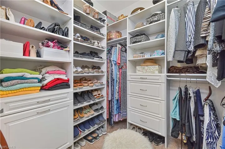 Custom walk-in closet featuring white cabinetry with brushed nickel hardware, extensive open shelving, multiple hanging rods, dedicated shoe racks, and built-in drawers for organized storage