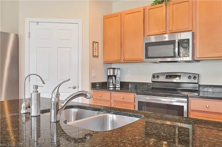 Kitchen featuring dark speckled countertops, stainless steel dual basin sink, stainless steel faucet, wood cabinetry, and stainless steel appliances