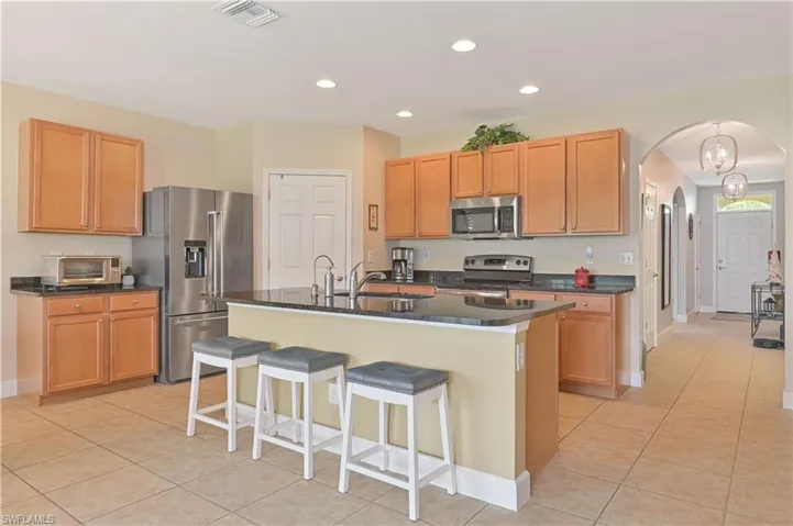 Kitchen featuring wood cabinetry, stainless steel appliances, dark countertops, and a central island with bar seating