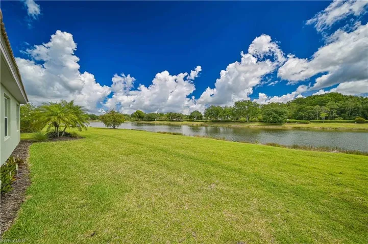 Expansive green lawn bordering a tranquil body of water, with a lush tree line on the opposing bank