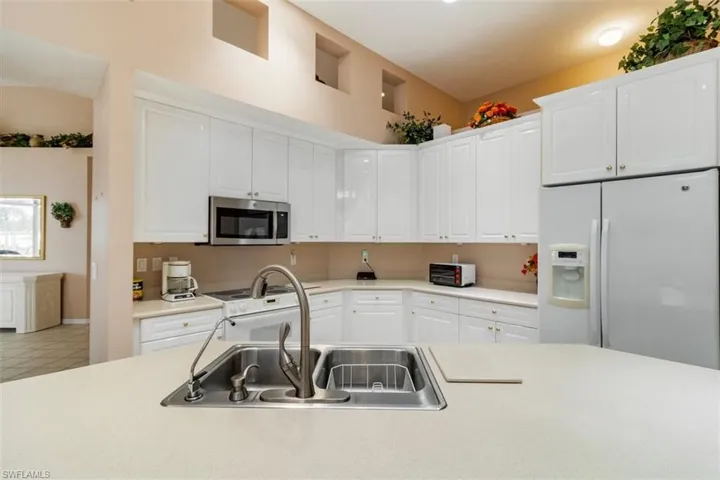 Kitchen with tile floors, sink, white appliances, and white cabinetry