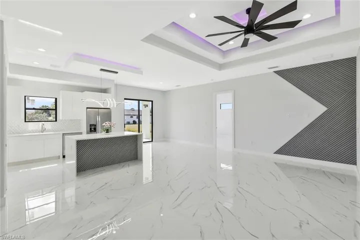 Unfurnished living room featuring recessed lighting, a raised ceiling, healthy amount of natural light, light marble finish floors, and ceiling fan