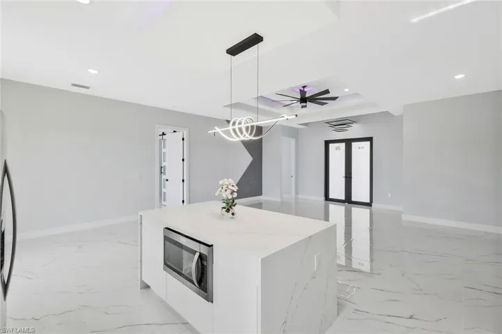 Kitchen with white cabinets, french doors, hanging light fixtures, stainless steel microwave, and modern cabinets