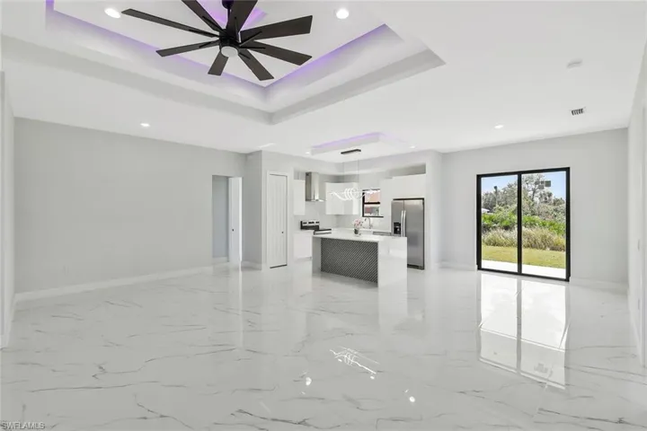 Unfurnished living room with recessed lighting, a raised ceiling, a ceiling fan, and light marble finish flooring
