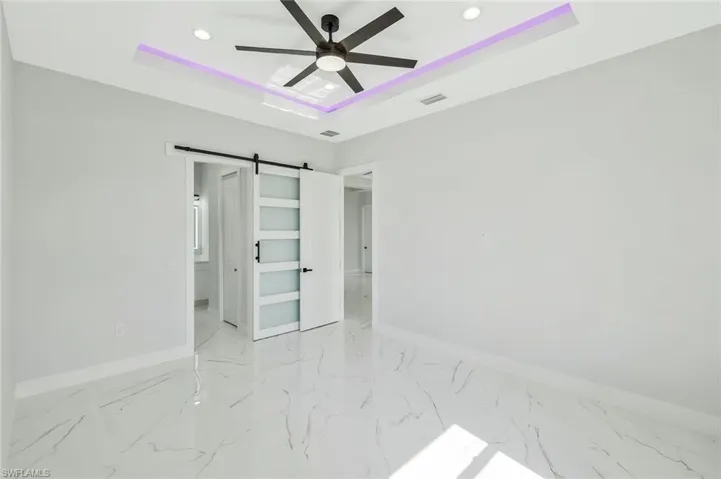 Unfurnished bedroom featuring a barn door, a raised ceiling, light marble finish floors, recessed lighting, and a ceiling fan