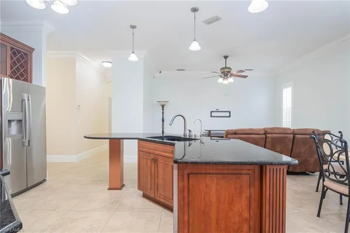 Kitchen featuring stainless steel fridge, a center island with sink, sink, and ornamental molding