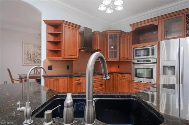 Kitchen featuring dark stone countertops, wall chimney exhaust hood, appliances with stainless steel finishes, and ornamental molding