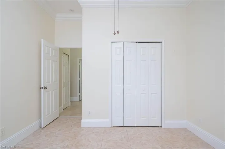 Unfurnished bedroom with ornamental molding, light tile patterned flooring, and a closet