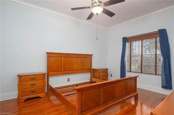 Bedroom with wood-type flooring, built in desk, ceiling fan, and crown molding