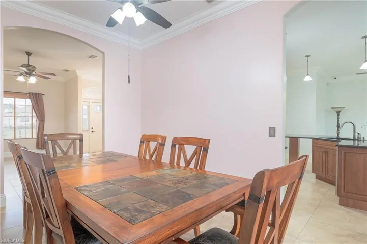 Dining area featuring light tile patterned flooring, ceiling fan, sink, and ornamental molding