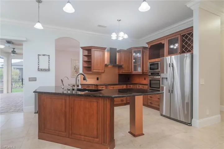 Kitchen with appliances with stainless steel finishes, dark stone countertops, wall chimney exhaust hood, crown molding, and pendant lighting