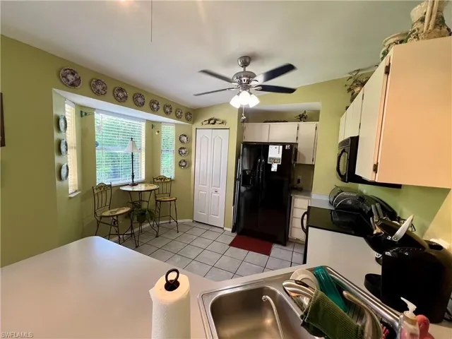 Kitchen featuring black appliances, white cabinetry, ceiling fan, and light tile floors