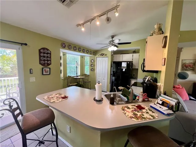 Kitchen featuring a breakfast bar, track lighting, black fridge with ice dispenser, and ceiling fan