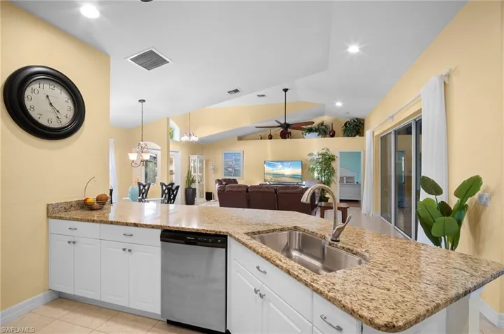 Kitchen featuring white cabinets, a ceiling fan, stainless steel dishwasher, light stone countertops, and a peninsula
