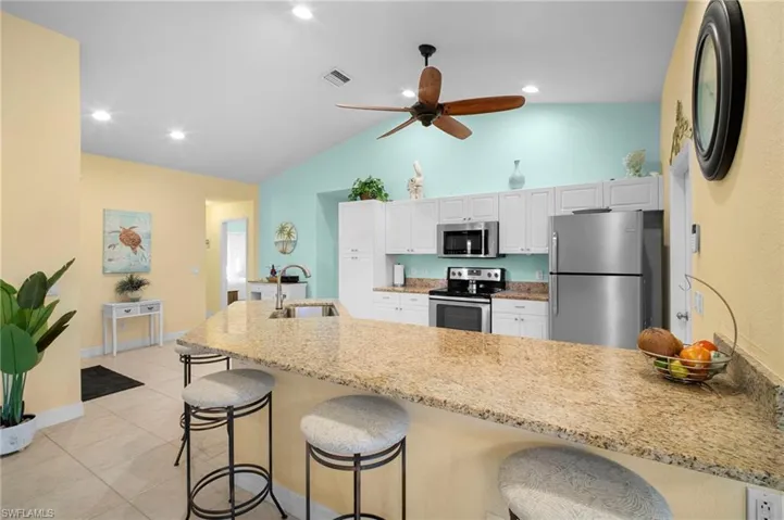 Kitchen with a kitchen breakfast bar, appliances with stainless steel finishes, a peninsula, light stone countertops, and white cabinetry