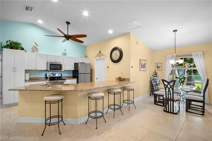 Kitchen with a peninsula, a breakfast bar, light stone counters, white cabinetry, and appliances with stainless steel finishes