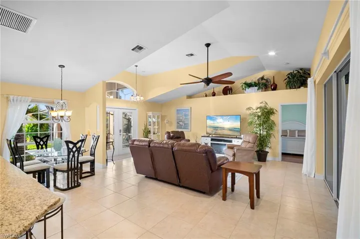 Living room with a chandelier, high vaulted ceiling, a ceiling fan, light tile patterned floors, and french doors