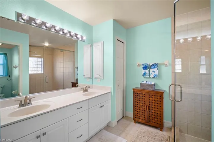 Full bathroom with double vanity, a stall shower, light tile patterned flooring, and a closet