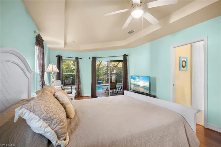 Bedroom featuring access to outside, a tray ceiling, wood finished floors, and ceiling fan