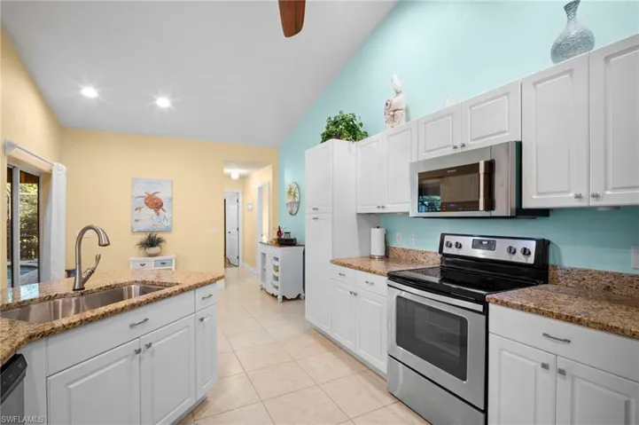 Kitchen featuring appliances with stainless steel finishes, white cabinetry, lofted ceiling, light stone counters, and a ceiling fan