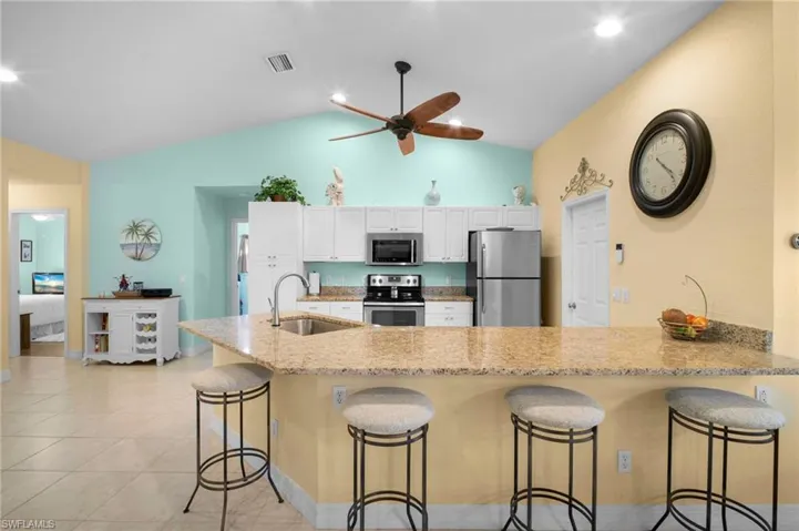 Kitchen featuring a peninsula, a breakfast bar area, appliances with stainless steel finishes, white cabinetry, and lofted ceiling