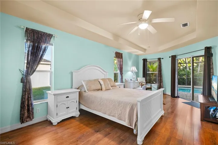 Bedroom with a tray ceiling, wood-type flooring, access to exterior, and a ceiling fan