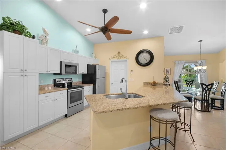 Kitchen with appliances with stainless steel finishes, white cabinetry, light stone countertops, high vaulted ceiling, and recessed lighting
