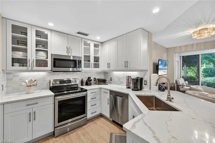 Kitchen with appliances with stainless steel finishes, tasteful backsplash, light stone countertops, light wood-type flooring, and recessed lighting