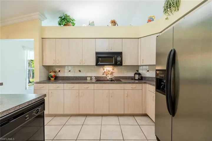 Kitchen with vaulted ceiling, decorative backsplash, stainless steel appliances, light tile patterned floors, and crown molding