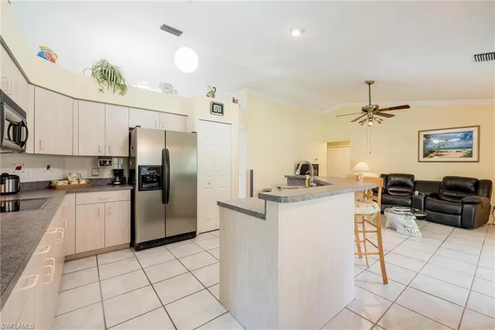 Kitchen with stainless steel appliances, lofted ceiling, ceiling fan, a center island with sink, and crown molding