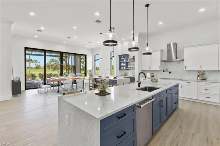 Kitchen with a large island, sink, white cabinetry, and wall chimney range hood