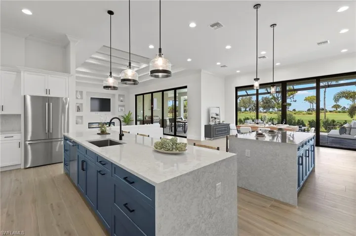 Kitchen with white cabinets, a large island with sink, sink, and stainless steel refrigerator