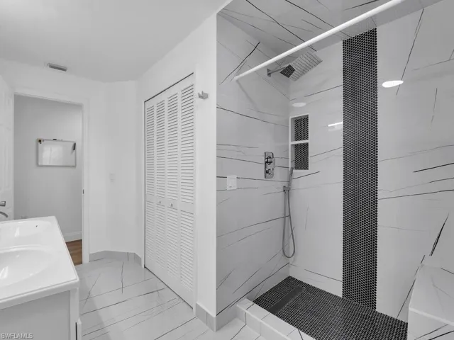 Full bath featuring tiled shower, double vanity, and a closet