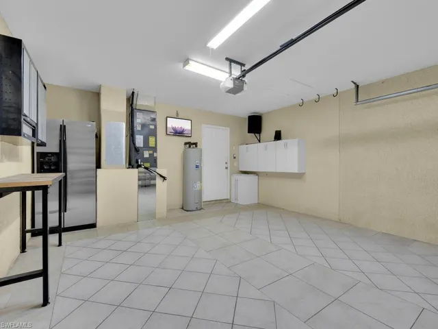 Garage featuring stainless steel fridge, electric water heater, a garage door opener, and heating unit