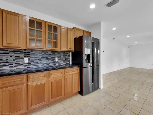 Kitchen with stainless steel refrigerator with ice dispenser, recessed lighting, backsplash, glass insert cabinets, and light tile patterned floors