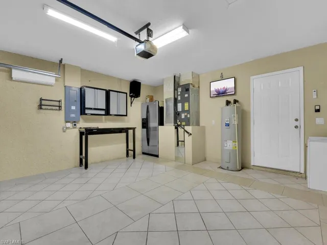 Garage featuring stainless steel fridge with ice dispenser, electric water heater, electric panel, a garage door opener, and a wall mounted air conditioner
