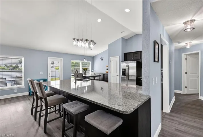 Kitchen with a breakfast bar, light stone countertops, lofted ceiling, dark wood-type flooring, and stainless steel fridge