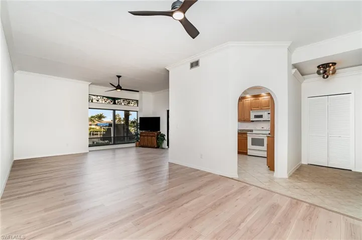 Unfurnished living room with ceiling fan, light wood-style floors, ornamental molding, and arched walkways