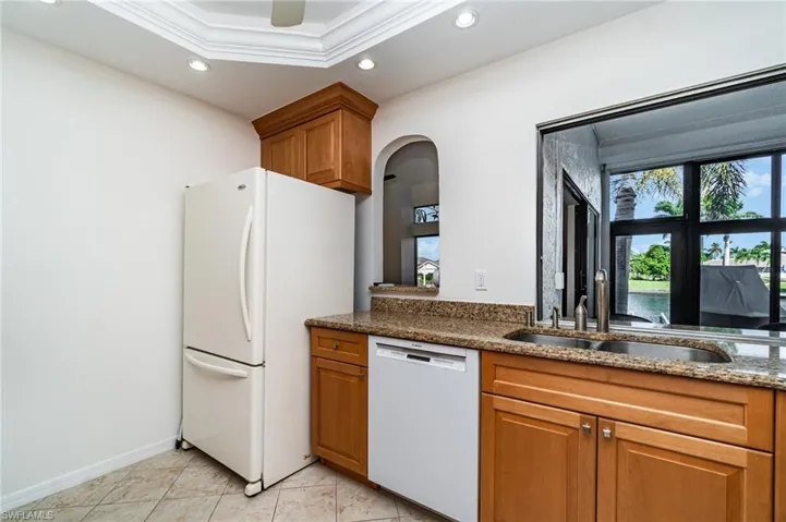 Kitchen featuring brown cabinetry, dark stone countertops, recessed lighting, white appliances, and crown molding
