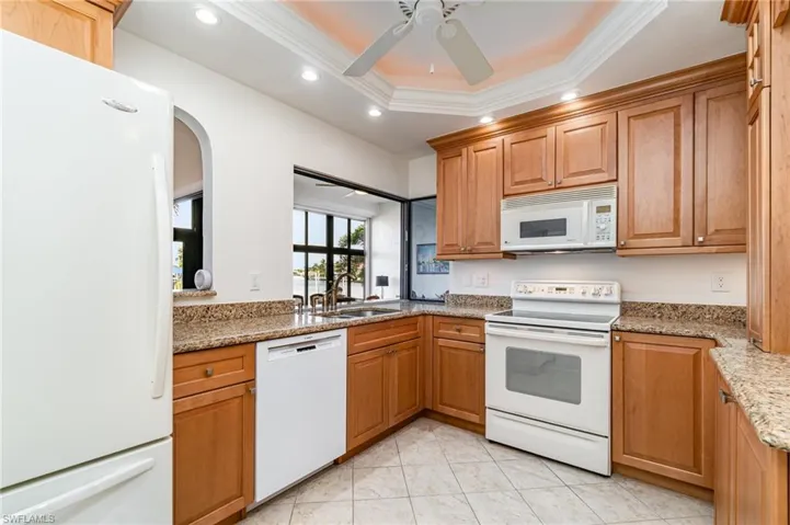 Kitchen featuring white appliances, light stone counters, a tray ceiling, recessed lighting, and arched walkways