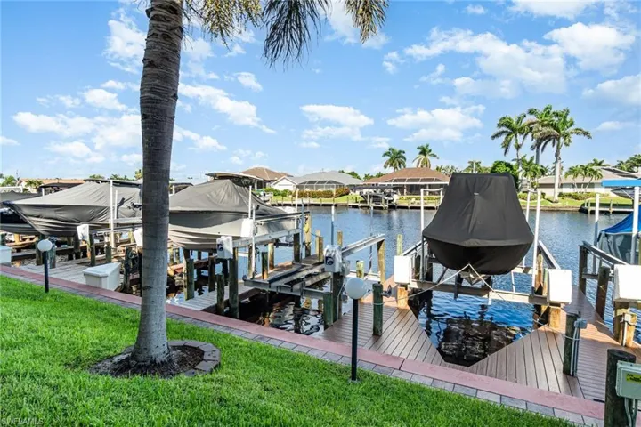 Dock area featuring boat lift, a water view, a lawn, and a residential view