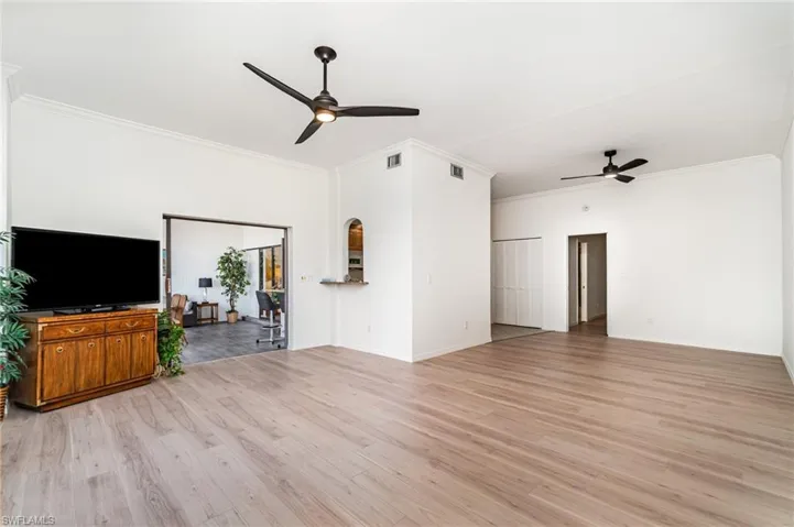 Unfurnished living room with light wood finished floors, crown molding, and ceiling fan