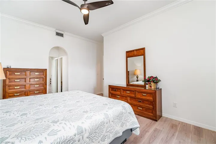 Bedroom with ornamental molding, light wood finished floors, arched walkways, and a ceiling fan