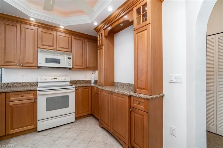 Kitchen featuring white appliances, glass insert cabinets, light stone countertops, recessed lighting, and crown molding