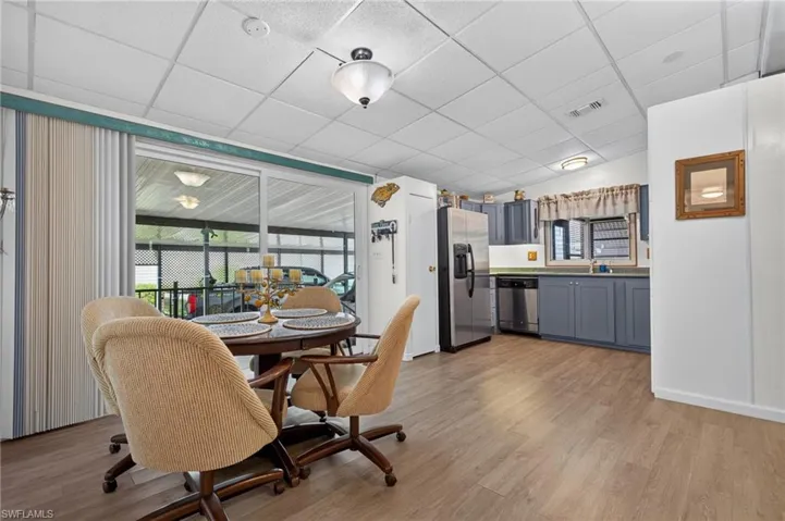 Open-concept kitchen and dining area featuring wood-finish flooring, stainless steel appliances, blue cabinetry with ample storage, and large windows with natural light