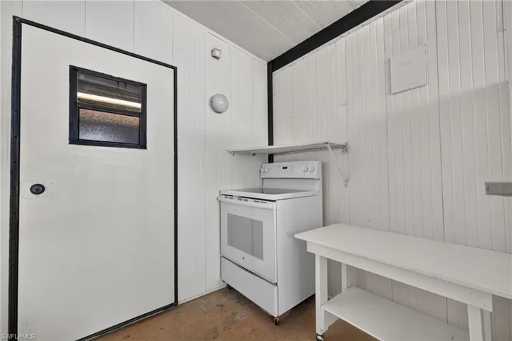 Outdoor stove - White paneled walls and ceiling, wall-mounted shelving, and a built-in white table