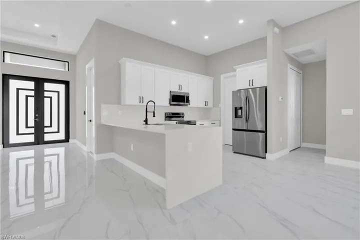 Kitchen featuring appliances with stainless steel finishes, white cabinets, light stone counters, a peninsula, and light marble finish flooring
