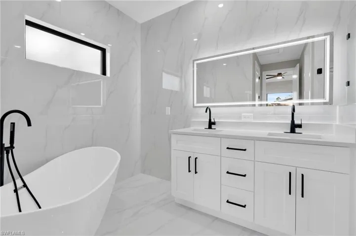 Full bathroom featuring double vanity, a soaking tub, light marble finish flooring, stone wall, and ceiling fan