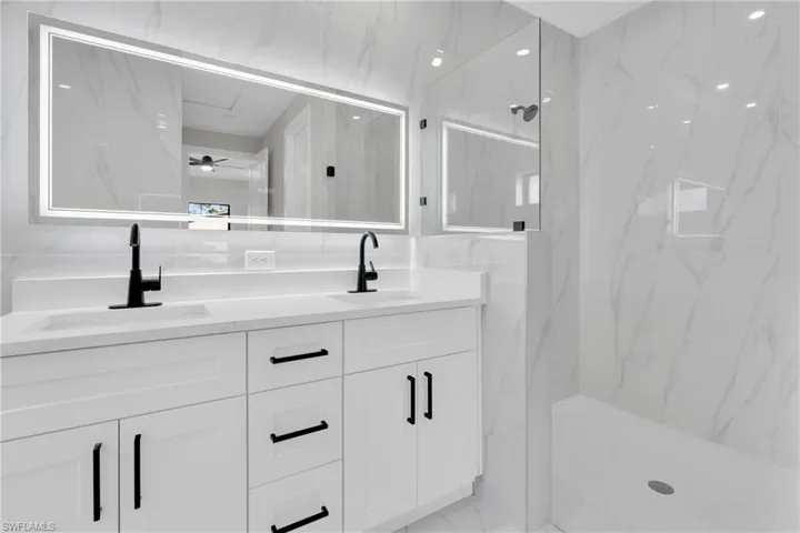 Full bath featuring double vanity, a ceiling fan, a marble finish shower, and light marble finish floors